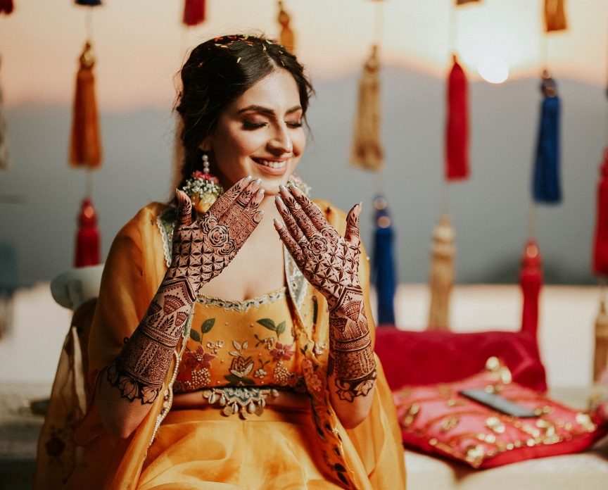 Photo of sisters and friends of the bride pose as the bride gets her mehendi  done