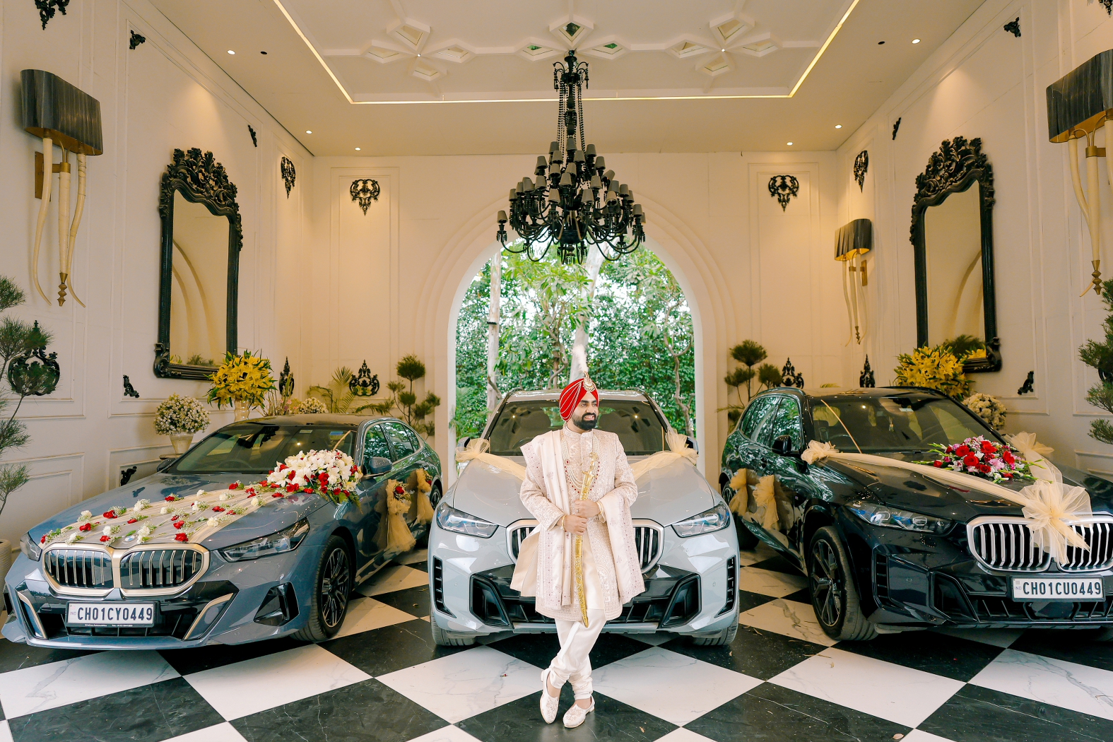 Groom posing in front of three luxury cars on his wedding day