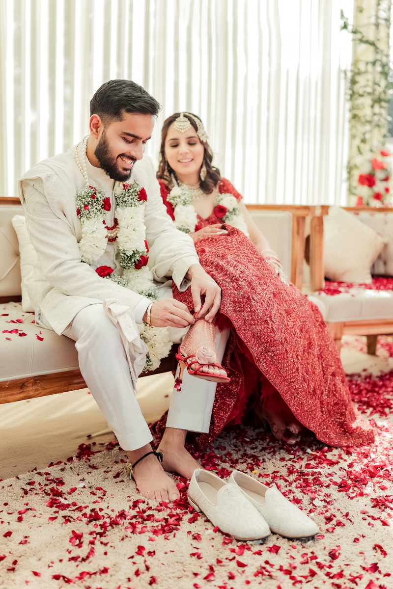 Couple caught in candid moment where groom is tying bride's shoes during their wedding ceremony
