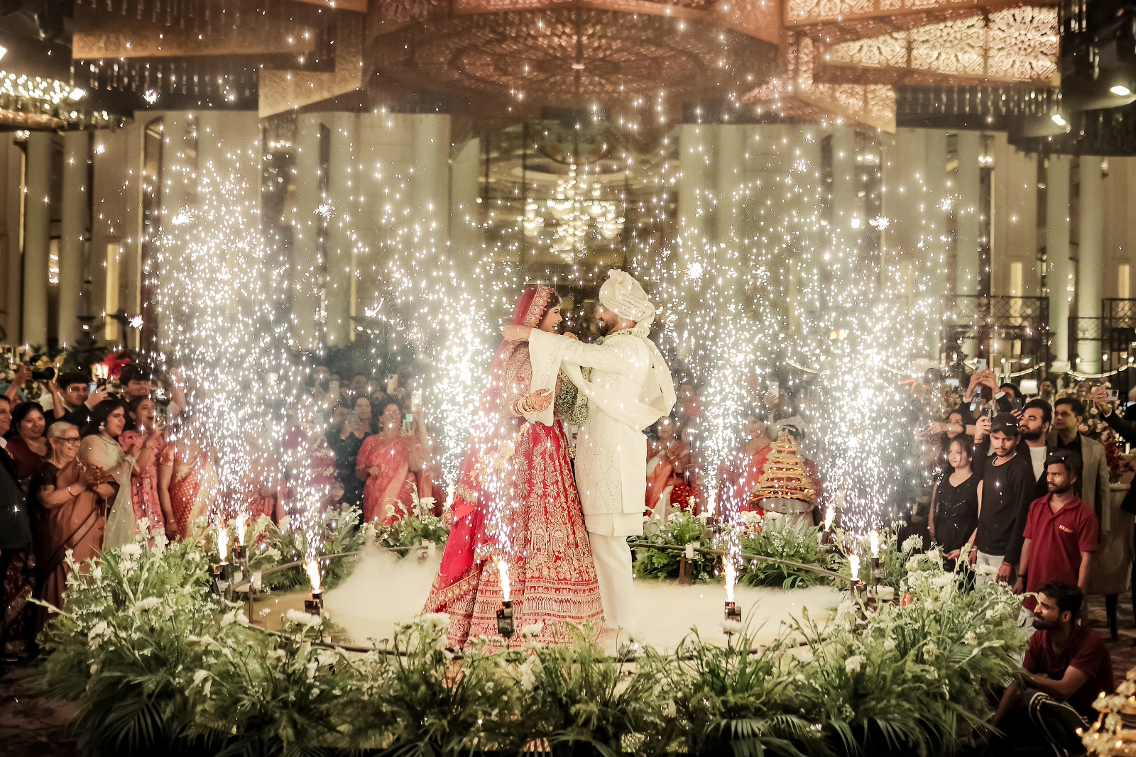 Candid shot of couple during varmala ceremony happening in a royal setup in aisle in between the venue with guests around