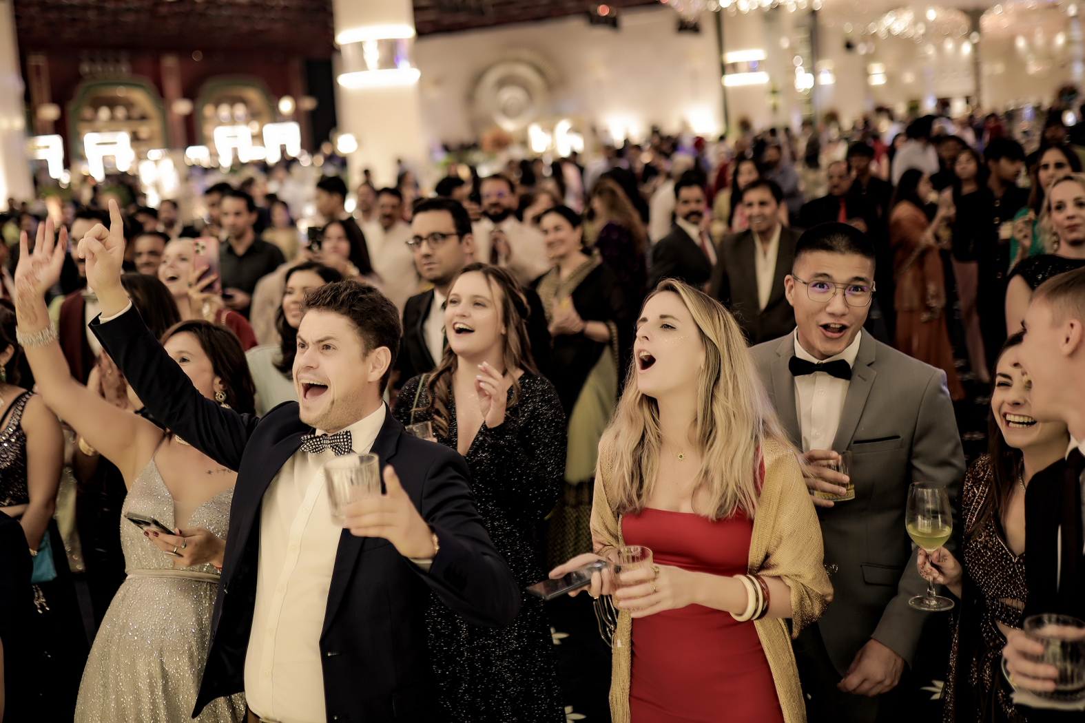 Cinematic wedding reception photograph of guests cheering and celebrating together under warm, ambient lighting. | Studio Memory Lane