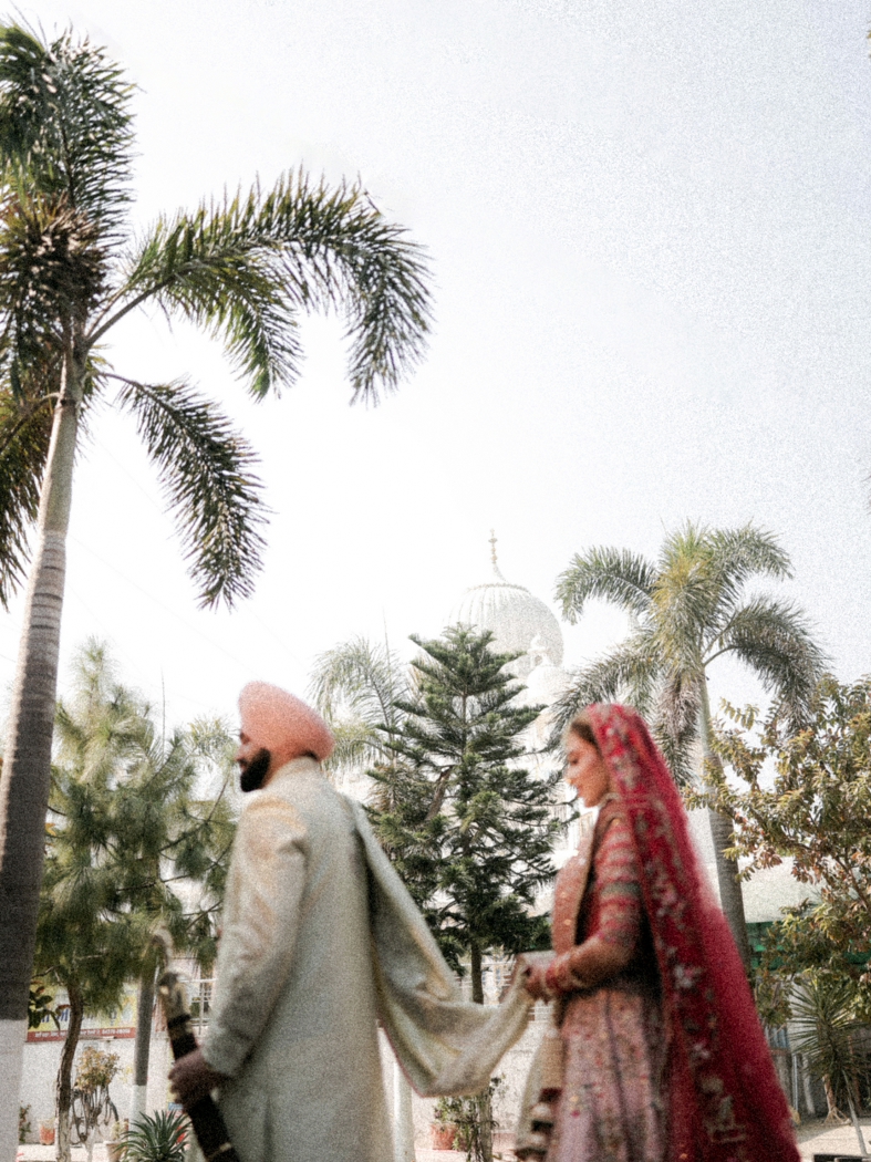 An editorial wedding portrait of a Sikh bride and groom standing outside the Gurdwara where they got married, holding the palla in a serene moment after their Anand Karaj ceremony.